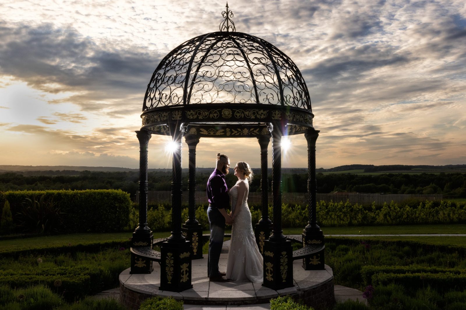 Couple standing under decorative gazebo at sunset