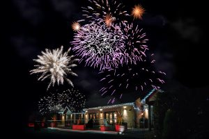 Fireworks display at night over a building with colorful explosions