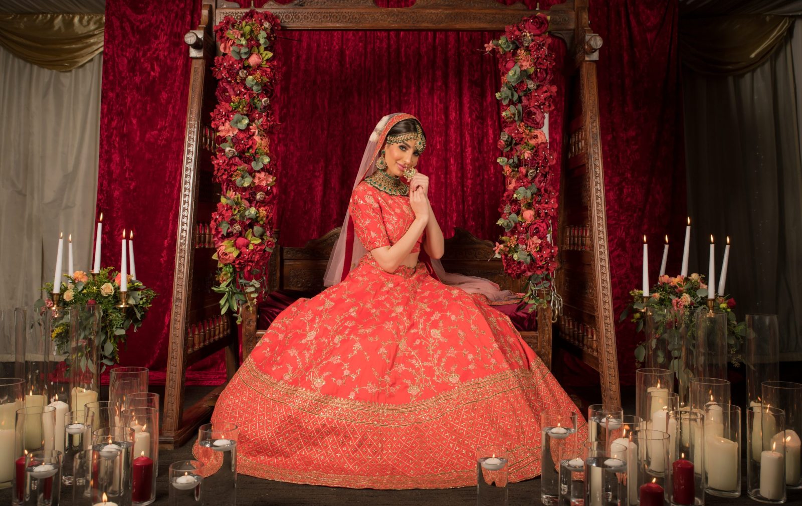 Bride in a traditional red lehenga seated on a floral stage surrounded by candles